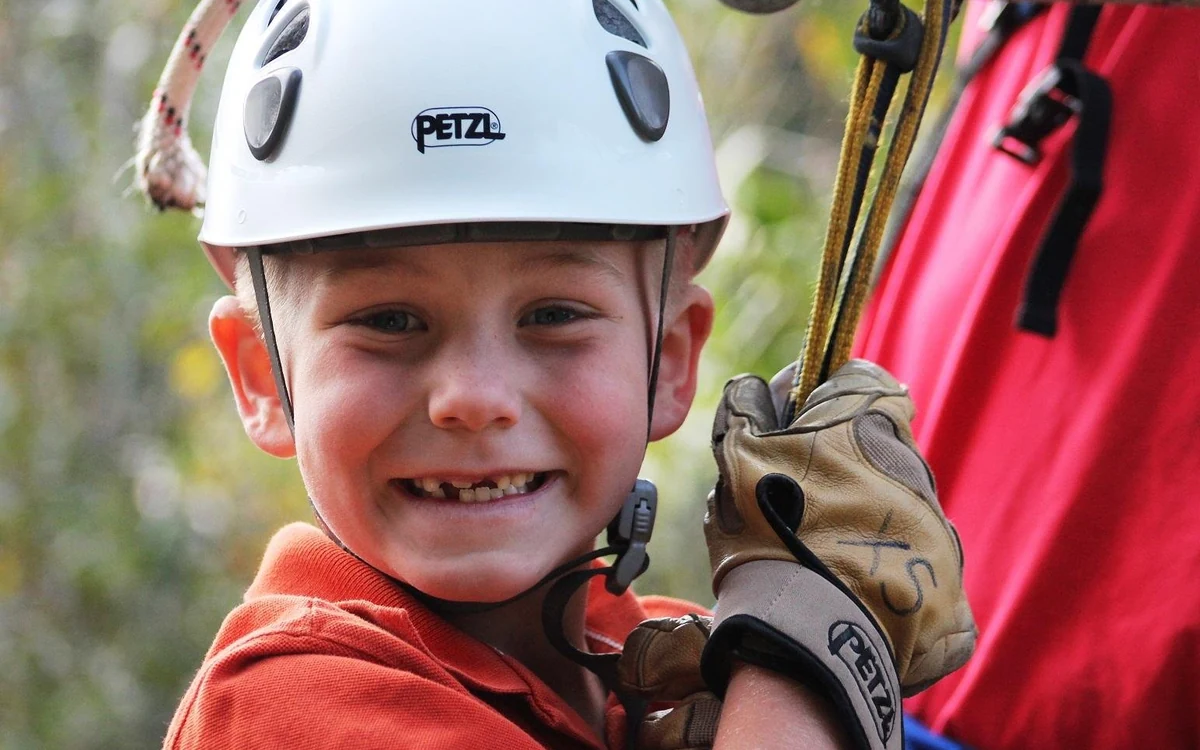 A young rider in a white helmet and leather gloves holding the zipline rope