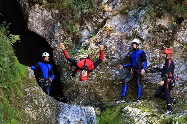Four people in wetsuits on a rope beside a narrow waterfall