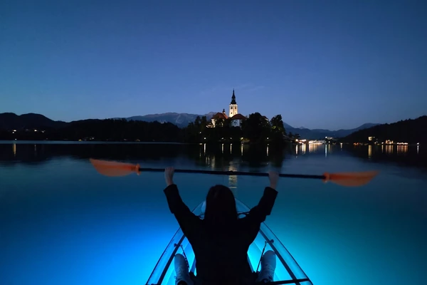 A clear kayak on Lake Bled at dusk, the island church lit behind it