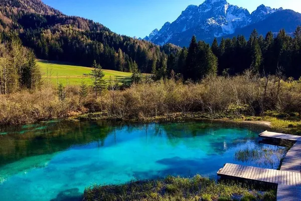 A turquoise spring pool with the Julian Alps behind it
